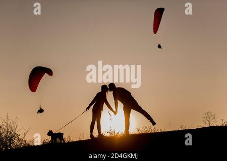 Une famille voyage avec son chien Schnauzer. Silhouettes sur fond de coucher de soleil. Famille à bord d'un voyage, regardez une mouche de parapente de jet de vapeur Banque D'Images