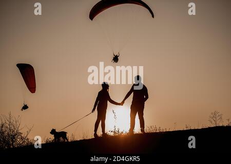 Une famille voyage avec son chien Schnauzer. Silhouettes sur fond de coucher de soleil. Famille à bord d'un voyage, regardez une mouche de parapente de jet de vapeur Banque D'Images