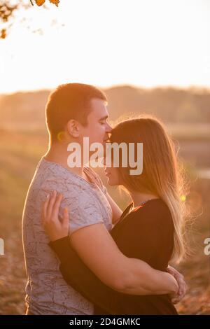 Jeune homme embrassant sur le front d'une belle fille blonde souriante aux cheveux longs. Portrait en gros plan d'un couple qui s'embrasse contre l'arrière-plan Banque D'Images