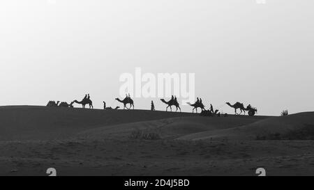 Une silhouette de mise au point sélective d'une ligne de chameaux marchant Sur les dunes de sable de Sam avec les gens qui les ont assis Banque D'Images