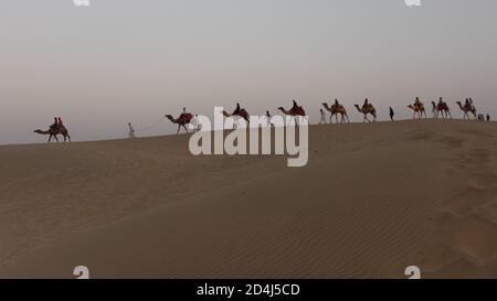 Une ligne de chameaux marchant sur les dunes de sable Sam avec les gens qui les ont assis Banque D'Images