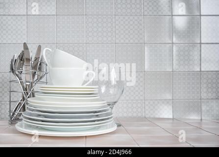 Une pile de assiettes en porcelaine blanche, de tasses à thé, d'un verre à vin, ainsi que des cuillères et des fourchettes dans le support pour les plats sur la table de cuisine contre le backgrou Banque D'Images