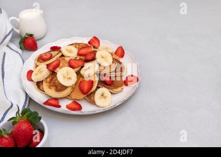 Mini crêpes tendance avec fraises et bananes sur une assiette blanche sur fond neutre avec espace pour le texte Banque D'Images