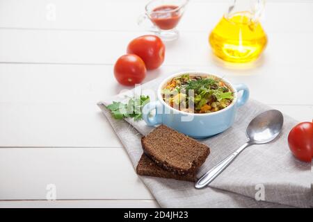 Soupe de haricots et d'olives aux herbes dans un bol en céramique, tomates, huile d'olive et pain sur une table en bois blanc. Copier les spaes Banque D'Images