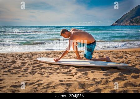 Homme cirant une planche de surf sur le sable avant le surf session Banque D'Images