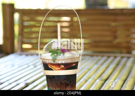 Café glacé mélangé à de la viande de coco dans une tasse en plastique transparent placée sur une table en bambou. Banque D'Images