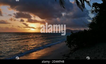 Coucher de soleil majestueux sur la mer se reflétant dans l'eau avec l'île de Praslin à l'horizon de la plage tropicale populaire Source d'argent, la Digue, Seychelles. Banque D'Images