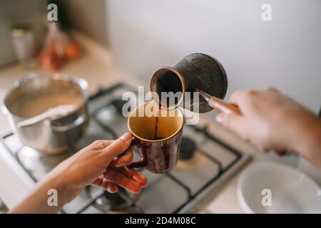 Le cliché en grand angle de la main d'une femme vient de se préparer café dans une cafetière turque dans une tasse Banque D'Images