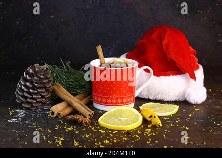 Composition de Noël. Tasse de Noël avec vin chaud chaud chaud, chapeau de Père Noël, cônes de sapin, branche d'épinette, bâtons de cannelle et anis étoilé sur fond sombre. Banque D'Images