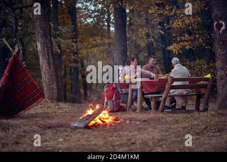 Un couple de personnes âgées et leur fille qui pique-nique la forêt autour d'un feu de camp sur un beau crépuscule d'automne Banque D'Images