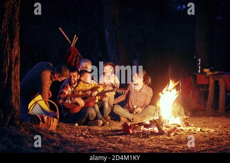 Une famille heureuse ayant un bon moment autour d'un feu de camp dans la forêt dans une belle nuit Banque D'Images