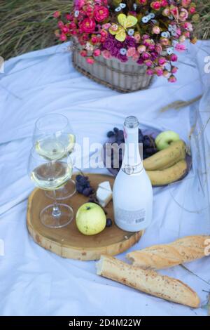 stand en bois avec deux verres de champagne et une bouteille, baguette, raisin et camembert sur une couverture blanche dans le champ. pique-nique Banque D'Images