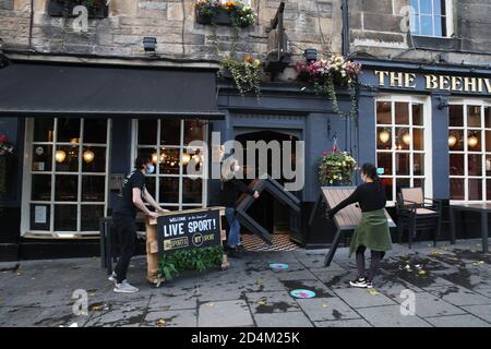 Les gens s'éloignent de l'hôtel Beehive Inn dans le Grassmarket, à Édimbourg, alors que les restrictions temporaires annoncées par le premier ministre Nicola Sturgeon pour aider à freiner la propagation du coronavirus sont entrées en vigueur vendredi à partir de 18 heures. Banque D'Images