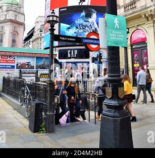 Personnes avec masques protecteurs devant la station de métro Piccadilly Circus avec signe de distance sociale, Londres 2020 Banque D'Images