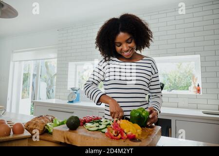 Jeune femme de race mixte coupant des légumes dans la cuisine à la maison, souriant et heureux Banque D'Images