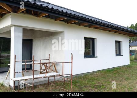 Une nouvelle couche de plâtre en silicone blanc sur le mur de la maison, échafaudage en métal visible et planches. Banque D'Images