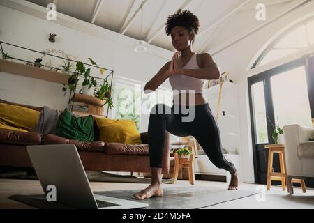 Prise de vue grand angle d'une jeune femme qui fait de l'entraînement à domicile ou du yoga à la maison, après un entraînement en ligne sur ordinateur ou en ligne Banque D'Images