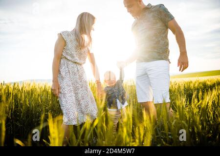 Bonne famille dans l'herbe verte lumineuse au coucher du soleil. Banque D'Images