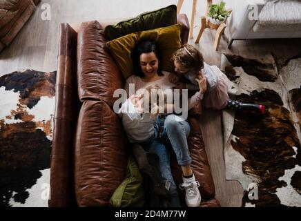 Mère jouant avec ses deux jeunes enfants gigling ensemble tout en étant allongé sur un canapé confortable dans la chambre familiale. Banque D'Images