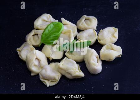 Raviolis frais au basilic sur fond noir et fleuri. Cuisine italienne maison saine concept.processus de fabrication des raviolis au pesto italien. Banque D'Images