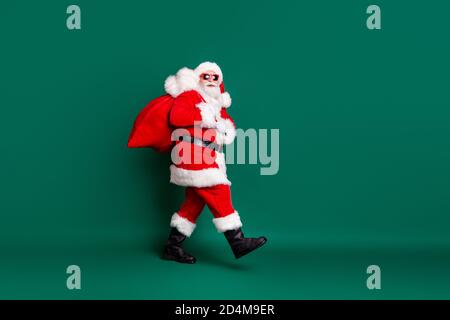 Photo de profil pleine longueur de la barbe grand-père du postier à la retraite sac de marche à porter présente porter robe de costume rouge de noël gants lunettes de soleil Banque D'Images