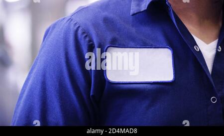 Homme méconnaissable portant une chemise uniforme bleue portant un nom vide étiquette ou étiquette blanche, identification du travailleur ou de l'employé. Banque D'Images