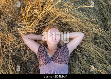 Belle jeune femme blonde se trouve dans la clairière parmi l'herbe sèche et regarde vers le haut. Vue de dessus. Le concept de bonheur et de détente Banque D'Images