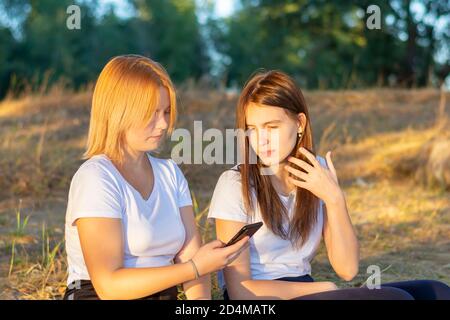 Deux amies regardent le téléphone dans le parc. Jeunes belles femmes dans les réseaux sociaux sur le smartphone en plein air en automne. Banque D'Images