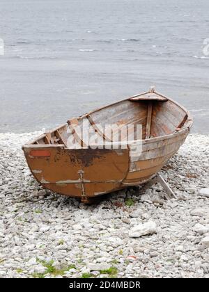 un petit bateau en bois brun ouvert pour la pêche vue de la poupe reposant sur la côte rocheuse avec la mer en arrière-plan. Banque D'Images