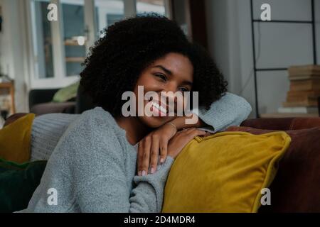 Femme de race mixte pensant à de bons souvenirs tout en étant assise sur le canapé à la maison souriant Banque D'Images