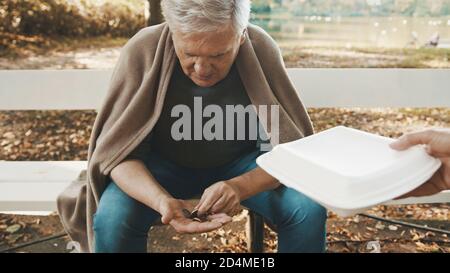 homme sans domicile âgé comptant des pièces. Recevoir un repas de charité d'un bénévole. Photo de haute qualité Banque D'Images