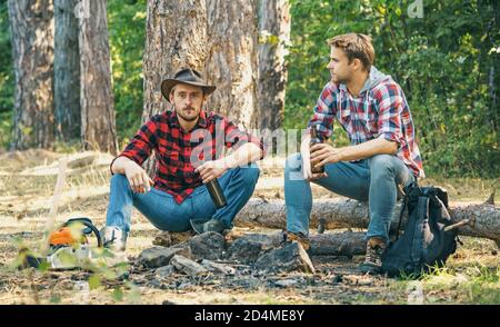 Les amis passent un week-end de loisirs dans la forêt. Deux heureux gens assis autour d'un feu de camp avec de la bière. Les amis apprécient le camp de week-end en forêt Banque D'Images