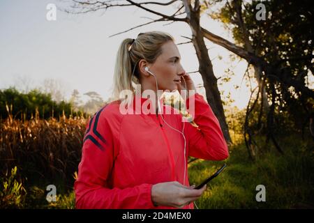 Belle femme avec écouteurs avant de commencer la course pendant lever du soleil Banque D'Images