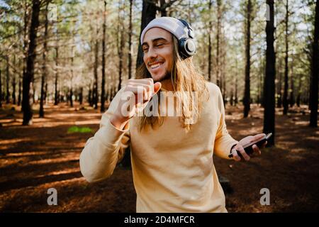 Jeune homme caucasien avec de longs cheveux jouant de la musique et de la danse avec des écouteurs dans le bois Banque D'Images