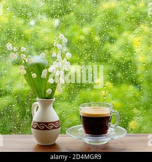 tasse de café et de lis de la vallée sur la fenêtre. La pluie tombe sur la fenêtre. Banque D'Images