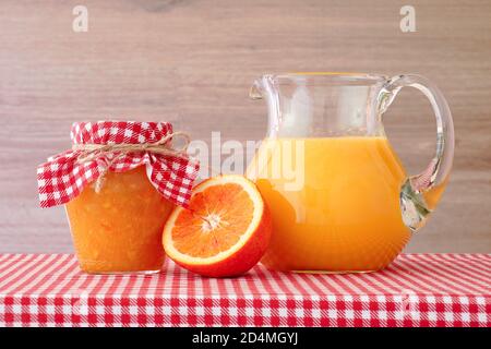 Jus d'orange, confiture, moitiés d'orange sur une nappe à carreaux rouges. Banque D'Images