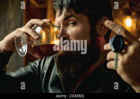 Homme avec la barbe tient le brandy de verre. Consommation de macho. Homme confiant avec des clés de voiture dans sa main. Ne conduisez pas en état d'ivresse. Arrêtez de boire. Banque D'Images