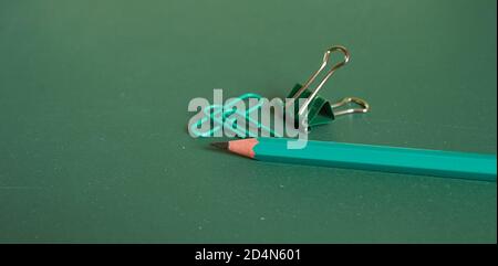 Un simple crayon et des trombones se trouvent sur un simple fond vert. Gros plan, macro Banque D'Images