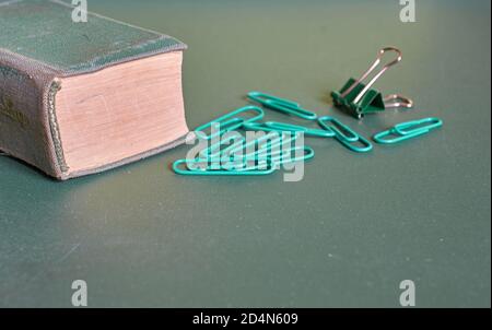 Un livre recouvert de vert et des trombones se trouvent sur un fond vert Uni. Gros plan Banque D'Images