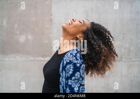 Portrait de la jeune femme afro-américaine confiante qui rit contre le mur gris. Banque D'Images