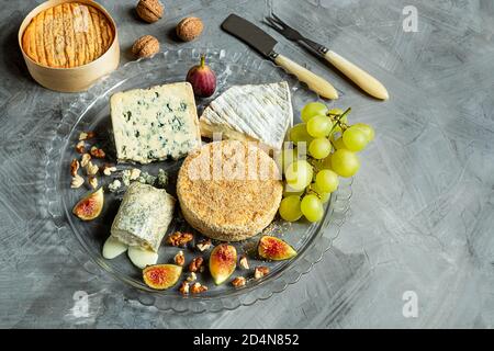 Assortiment de fromages français - camembert, roquefort, brie, fromage de chèvre et epoisse avec raisins, figues et noix sur fond gris. Vue de dessus, copier la flèche Banque D'Images