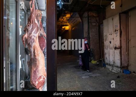 Une femme palestinienne portant un masque facial en raison de la pandémie du coronavirus COVID-19 passe devant un boucher dans la vieille ville du quartier musulman Jérusalem-est Israël Banque D'Images