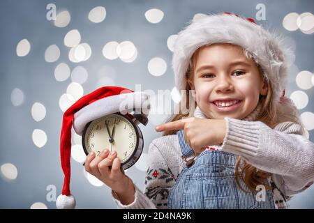 Veille de Noël ! Un enfant joyeux dans un chapeau de Noël avec réveil Banque D'Images