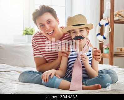 Drôle de temps. Bonne journée pour les pères ! Papa et sa fille jouent à la maison. Jolie fille tient la moustache en papier sur le bâton et fait semblant de papa. Banque D'Images