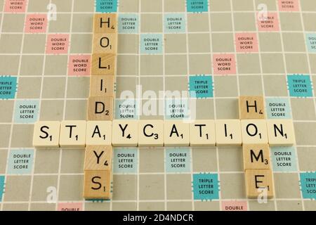 Staycation, expression sur un scrabble en blanc avec les mots vacances et la maison en tuiles de bois marron Banque D'Images