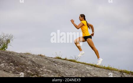 Vue latérale d'une femme de fitness qui fait de la course à haute intensité sur le flanc de la montagne par la mer Banque D'Images