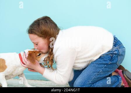 Gros plan portrait jeune fille, embrassant son bon chien d'ami sur fond bleu. La petite fille embrasse le chien dans le nez. Banque D'Images