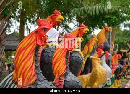 Une grande statue de coq en céramique portant un masque facial protecteur, parmi un groupe de grandes statues de coq religieuses Banque D'Images