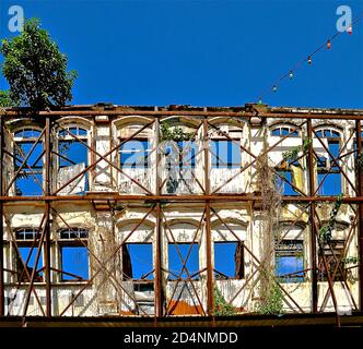 Bâtiment abandonné surcultivé avec des plantes et des arbres, soutenu par des échafaudages rouillés. Banque D'Images