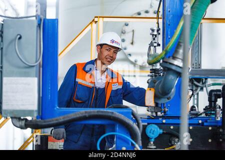 Shymkent, Kazakhstan-avril 26 2012 : usine de production moderne d'huile moteur. Souriant, jeune ouvrier asiatique, tuyaux et équipement. Arrière-plan flou. Banque D'Images